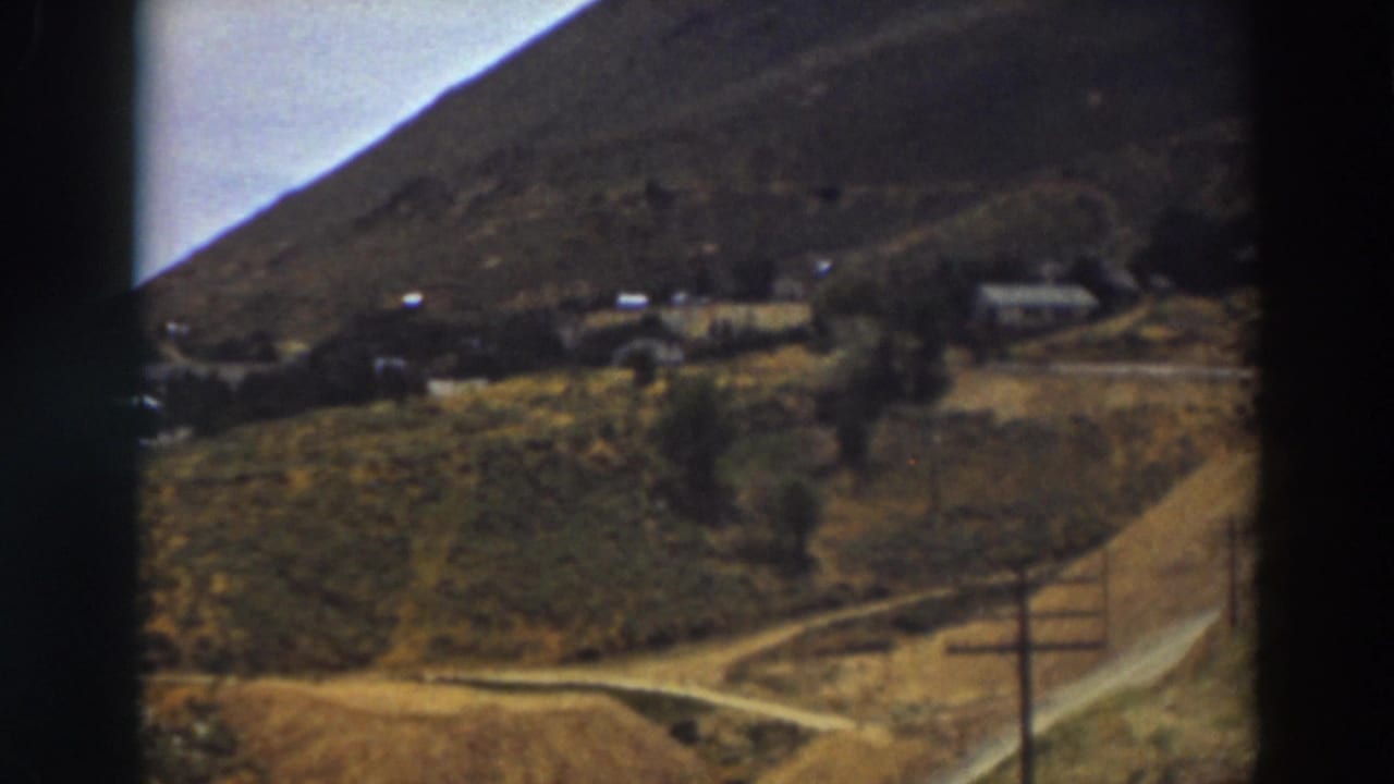 Distant hillside settlement with dirt roads, utility poles, and scattered houses.