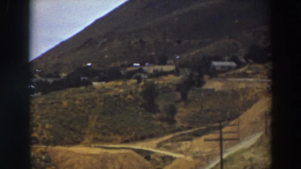1937 Truckee, California home-movie frame showing a rural hillside settlement, dirt roads, utility poles, and scattered buildings.