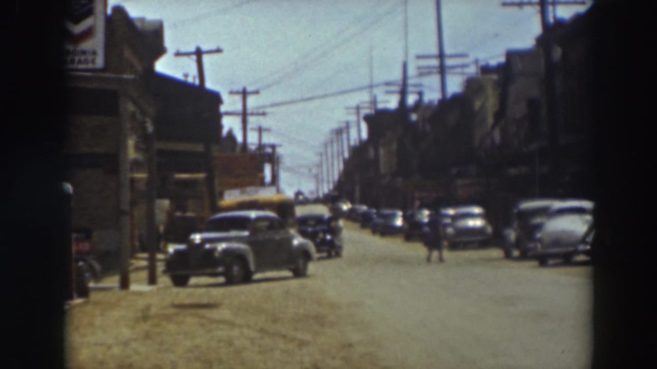1937 Truckee street scene with classic parked cars, storefronts, overhead wires, utility poles, and small distant figures in the roadway.