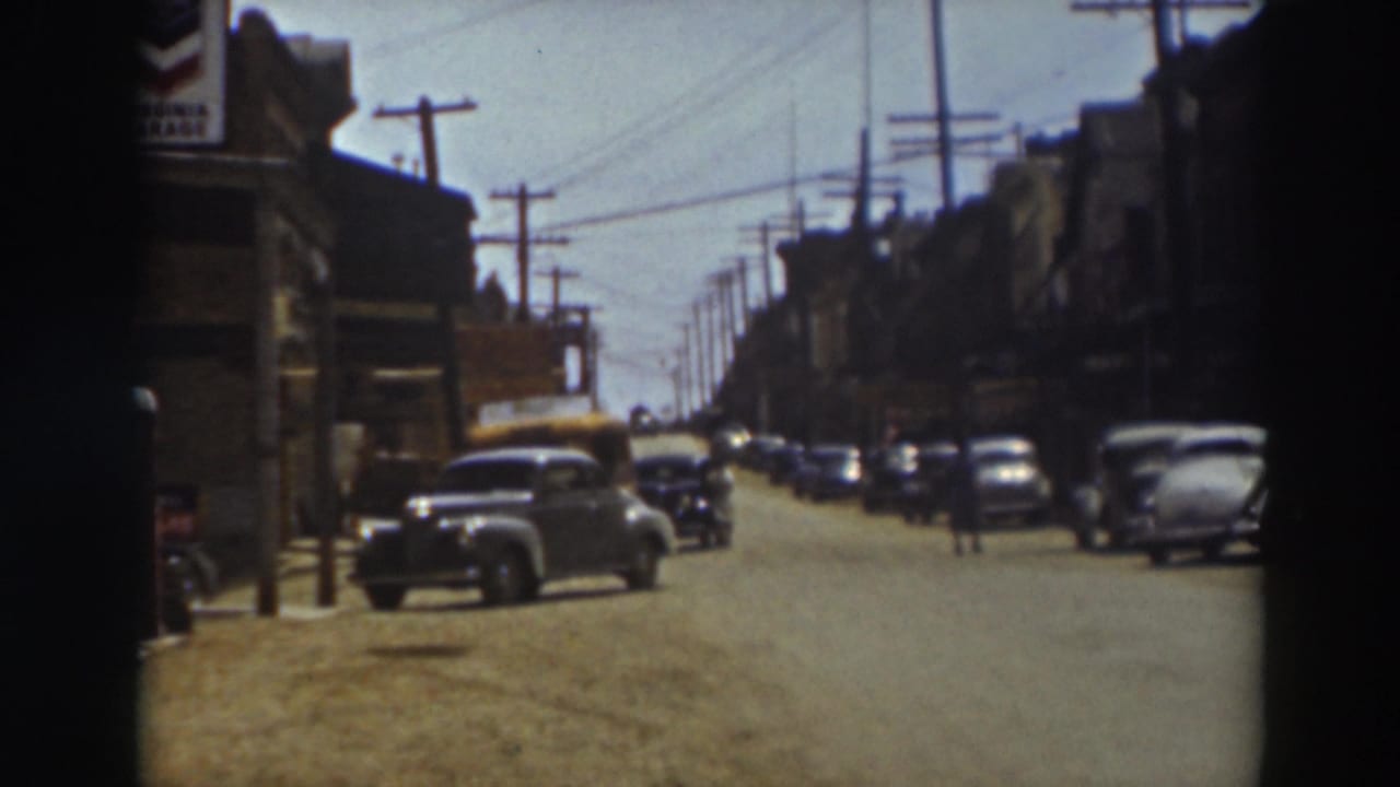 1937 Truckee street view with parked late-1930s cars, storefronts, overhead wires, and a few distant pedestrians.