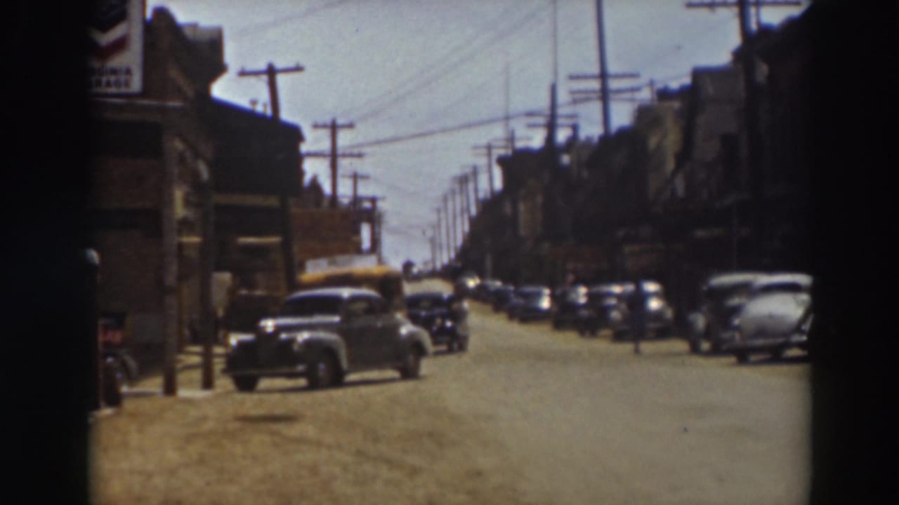 A 1937 Truckee street scene shows cars parked along both sides, storefront shadows, utility poles, and small figures in the road.