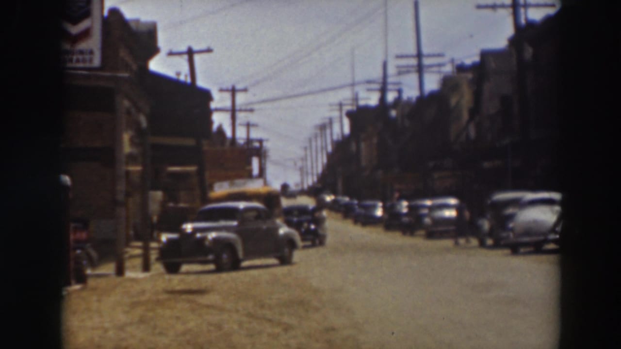 The home-movie frame looks down a Truckee commercial street with parked cars, awnings, telephone poles, and distant pedestrians.