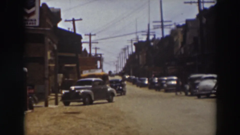 The home-movie frame looks down a Truckee commercial street with parked cars, awnings, telephone poles, and distant pedestrians.