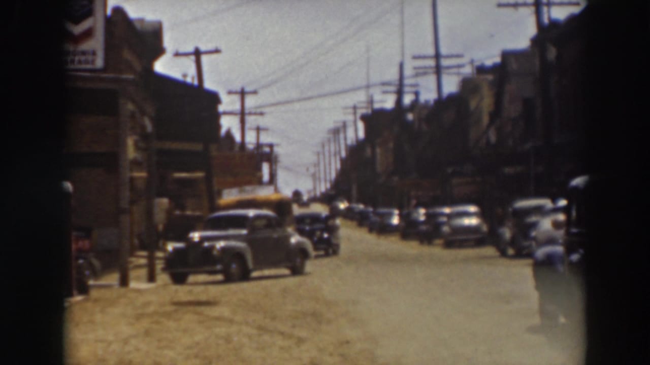 1937 Truckee street view with parked automobiles, commercial buildings, overhead wires, and a yellow bus approaching from farther down the road.