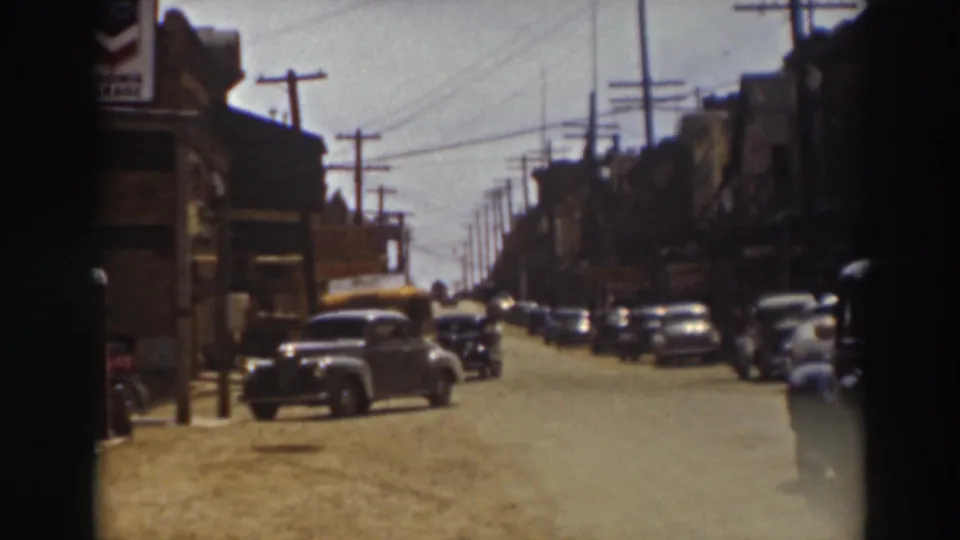 1937 Truckee street view with parked automobiles, commercial buildings, overhead wires, and a yellow bus approaching from farther down the road.