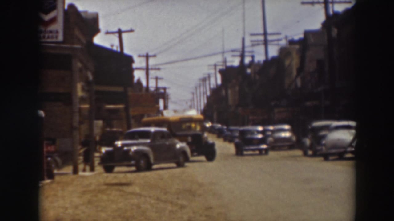 1937 Truckee street scene with a yellow bus traveling through the frame past parked automobiles and early commercial buildings.