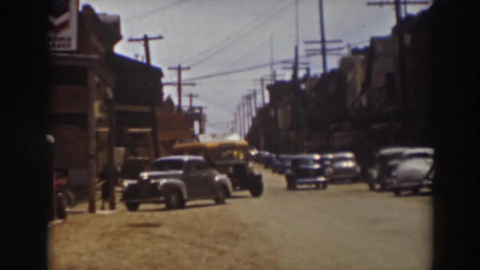 1937 Truckee street scene with a yellow bus traveling through the frame past parked automobiles and early commercial buildings.