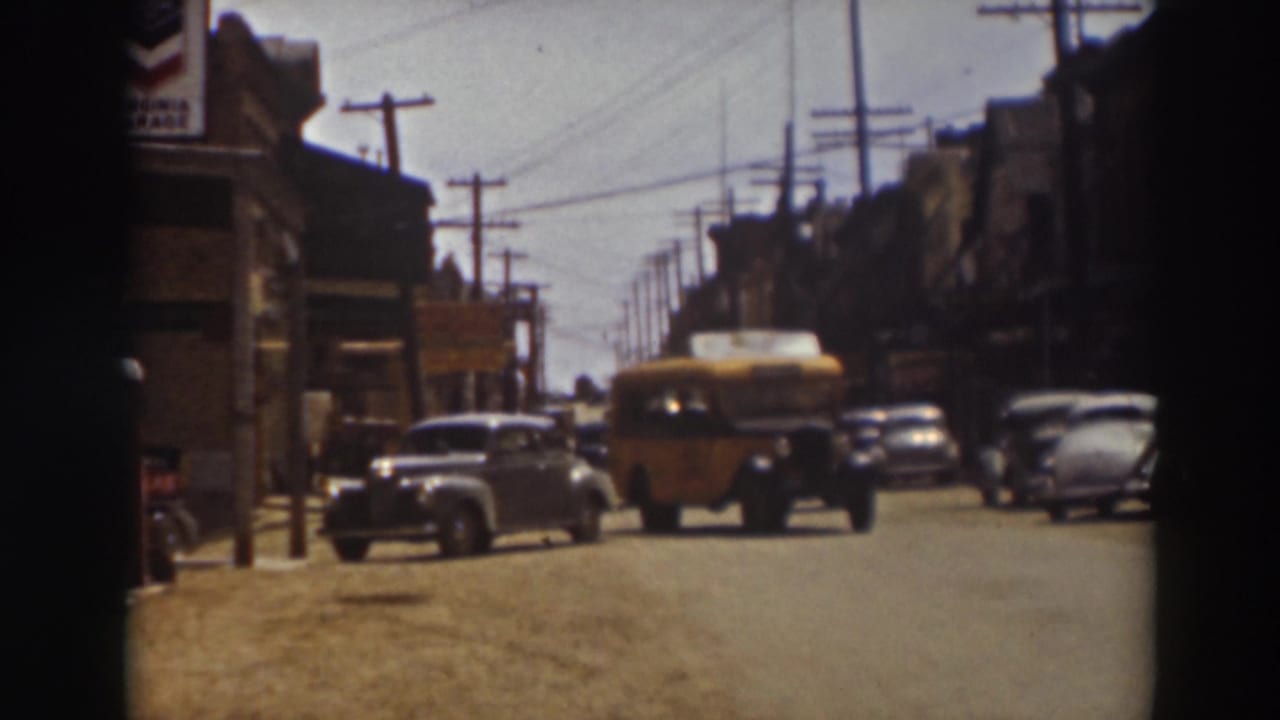 1937 Truckee street view with the yellow bus near the foreground, classic cars parked along both sides, and overhead utility lines above.