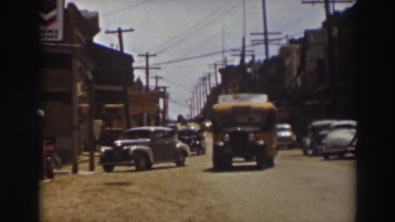 Yellow school bus approaches the camera on a Truckee, California street, with 1930s cars, storefronts, utility poles, and wires in view.