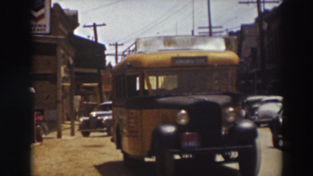 The yellow bus moves closer on a Truckee street, with dark parked cars, storefronts, utility poles, and overhead wiring visible.
