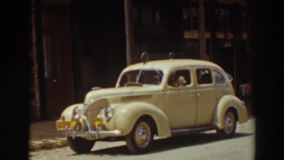 Home-movie frame from Truckee in 1937 showing the parked sedan closer in the contact sheet, with the dog still at the window.