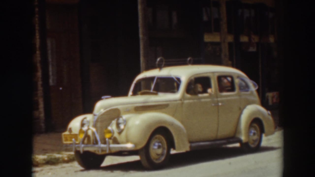 Cream-colored vintage sedan parked on a street with a person visible inside.