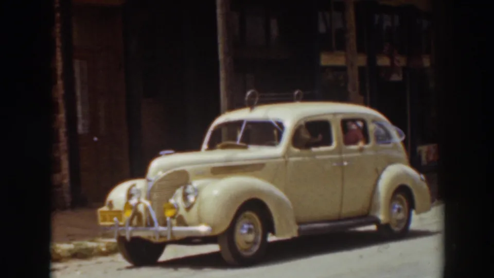 Cream-colored 1930s-style car on a Truckee street, with a person and possible dog visible inside the cabin.
