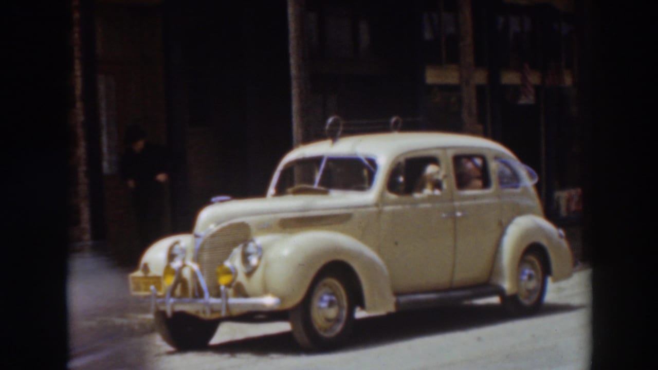 Cream-colored vintage sedan parked at a curb on a sunlit street.