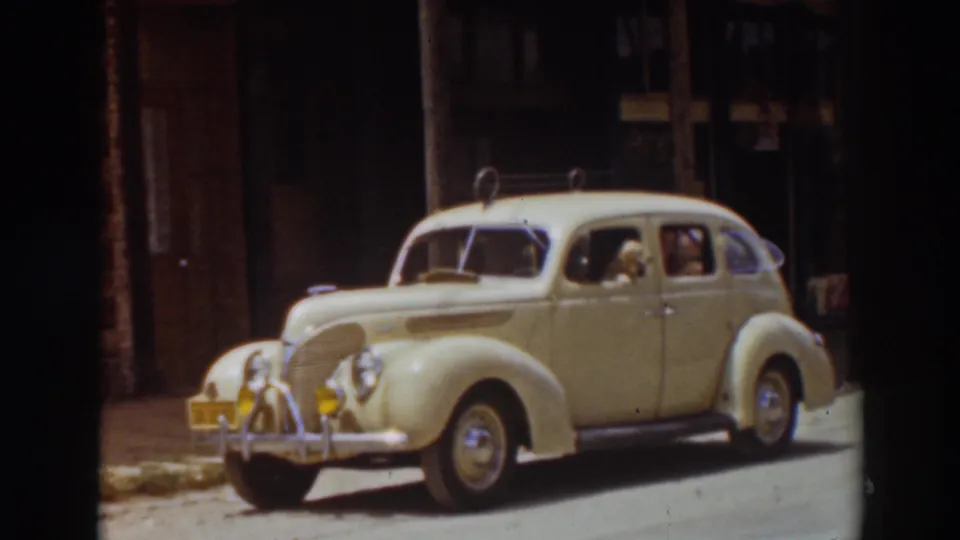 The classic sedan is shown more closely at the curb, with its rounded fenders, chrome trim, and occupant visible in the 1937 Truckee street scene.