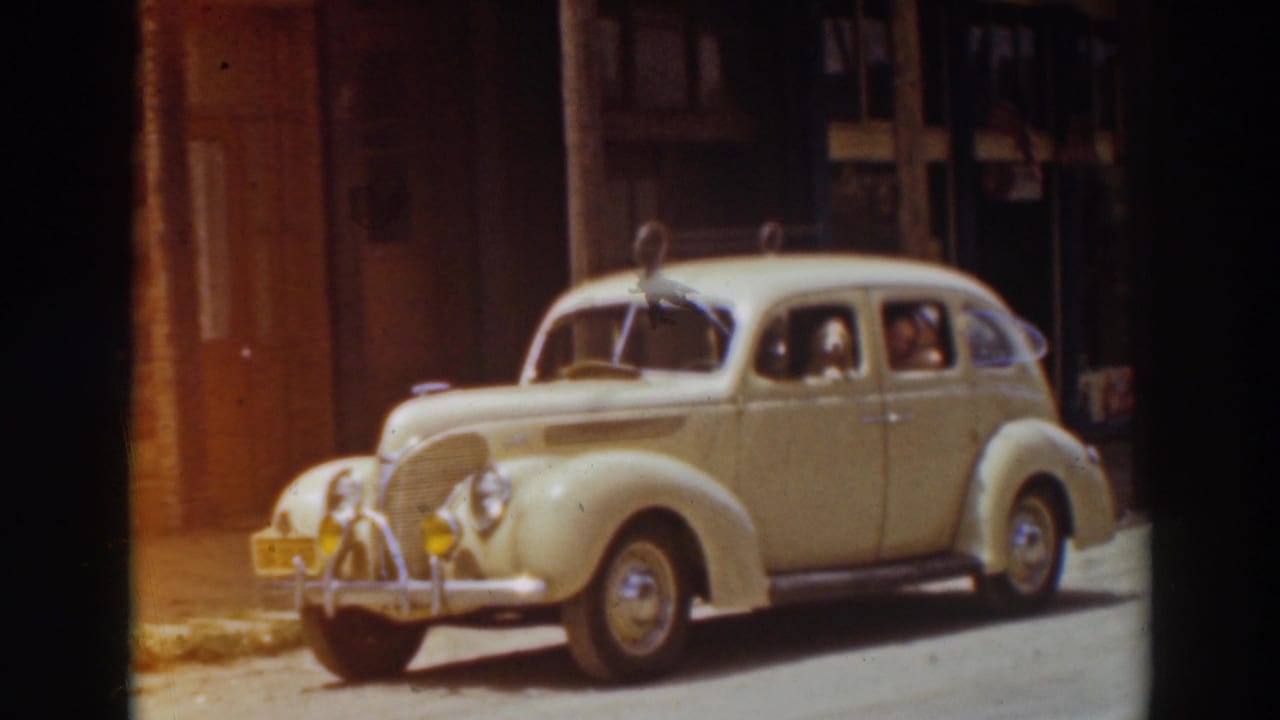 Cream-colored sedan parked on a Truckee street in 1937, with brick buildings and warm 8mm film color.