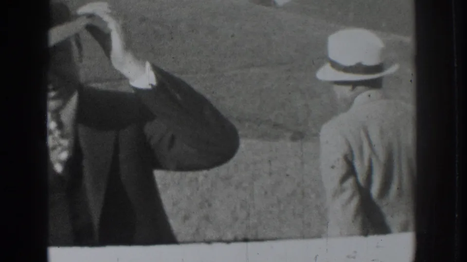 Two adult men in period suits and brimmed hats stand outdoors in the 1937 Vacaville home-movie frame, one partly cropped while touching his hat.