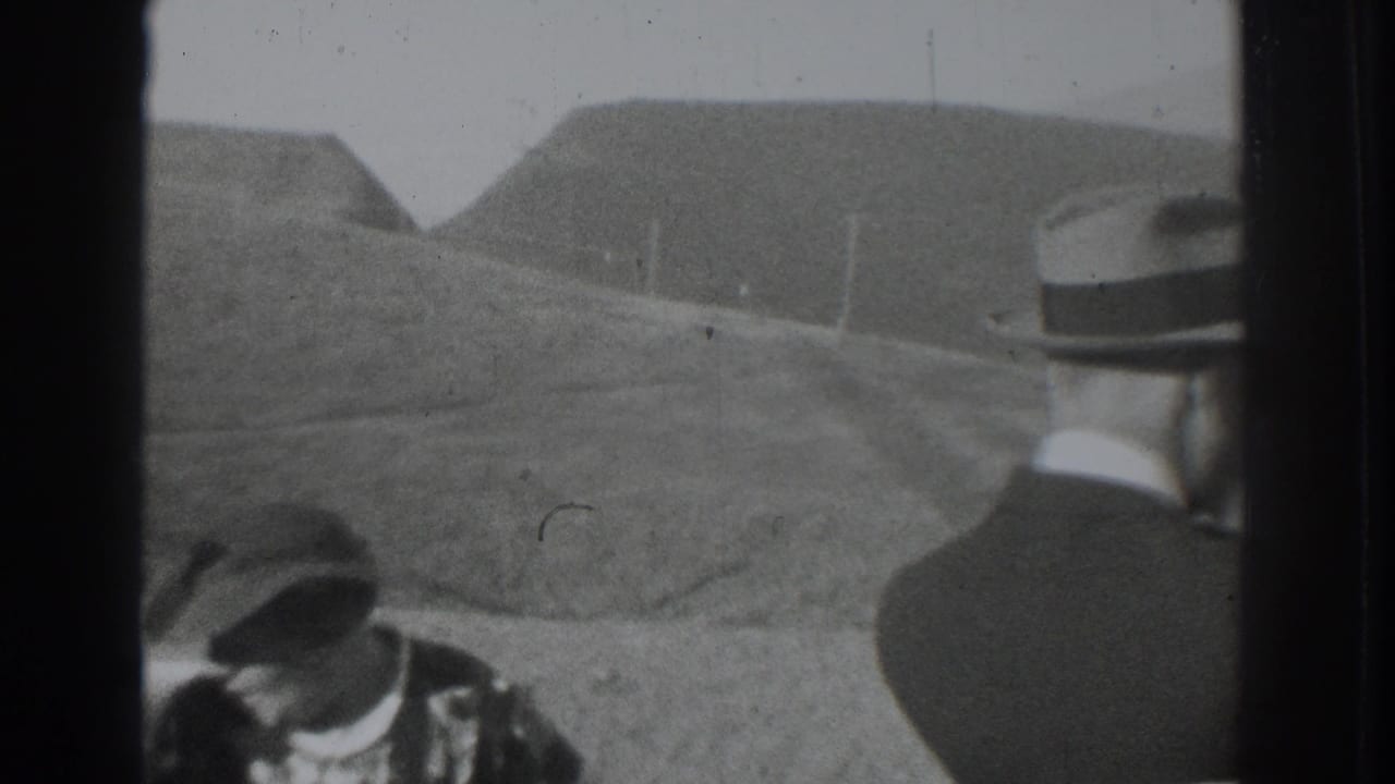 1937 Vacaville home-movie frame with two adult men in hats near a vehicle, backed by rolling hills and a dirt road.