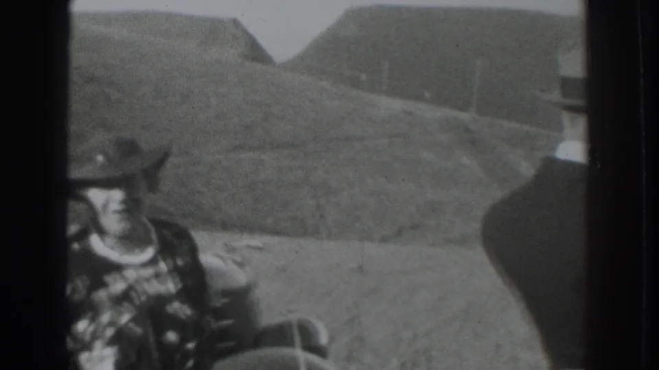 A man in a hat and patterned shirt sits near a vehicle in 1937 Vacaville footage, with hilly open country behind him.