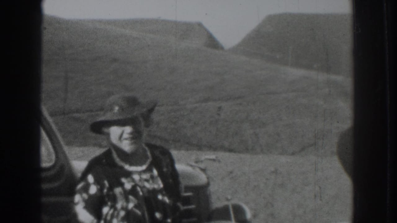 Woman in a wide-brimmed hat smiles beside a vehicle with hills behind her.