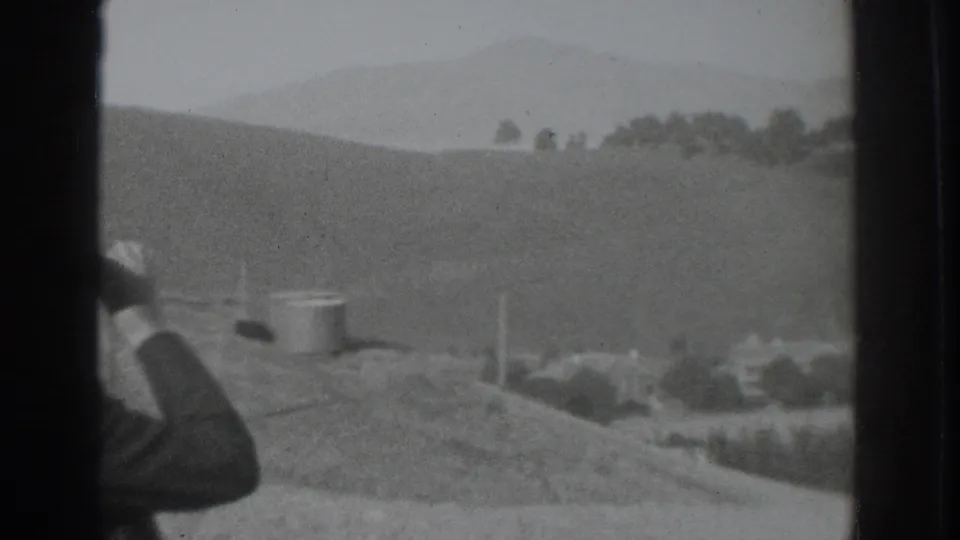 The camera looks past the edge of a man in a hat toward rolling hills, a roadside area, and distant trees near Vacaville.