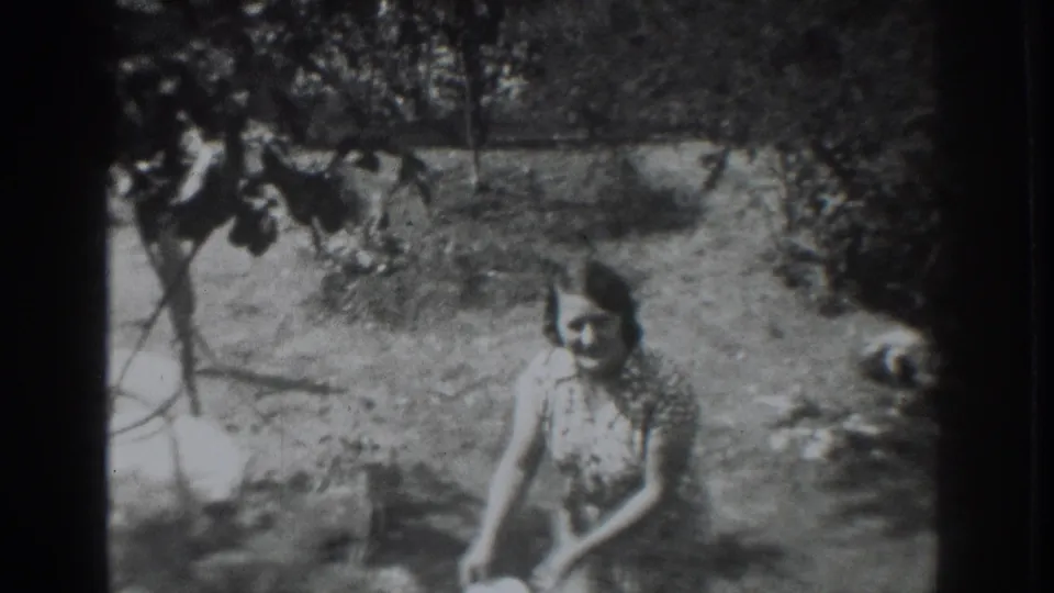 A woman in a patterned dress crouches in a 1937 Vacaville yard, holding a white scoop near the ground.