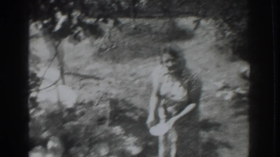 1937 Vacaville home-movie frame showing a woman in a patterned dress holding a light bowl among grass and trees.