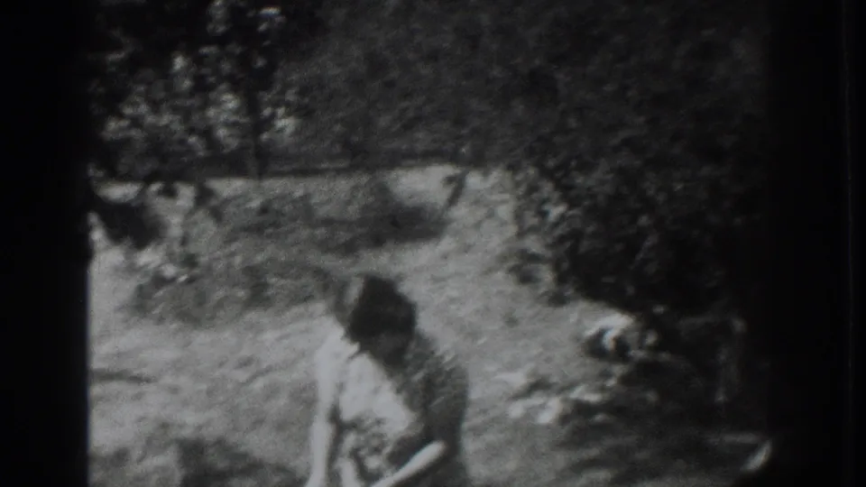 1937 Vacaville frame with a woman leaning toward a light bowl in a grassy, tree-shaded yard.