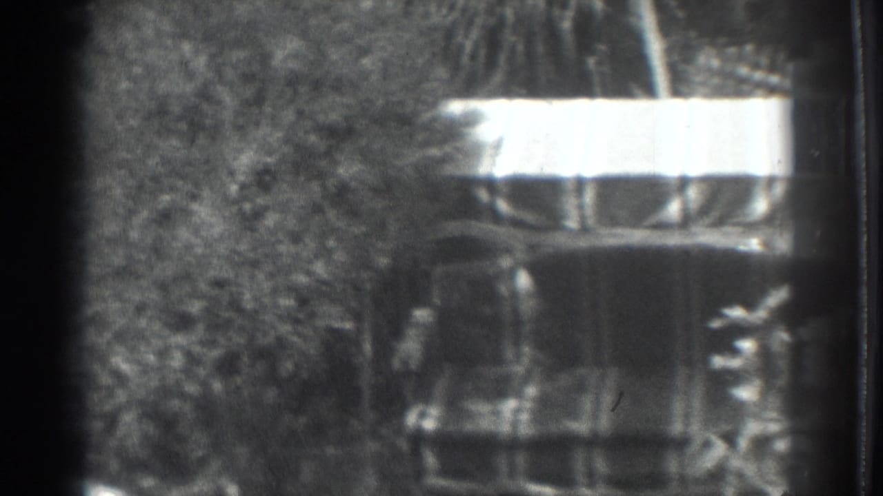 1937 Vacaville 8mm frame with trees, brush, and a bright-topped shaded structure or object in a rural outdoor setting.