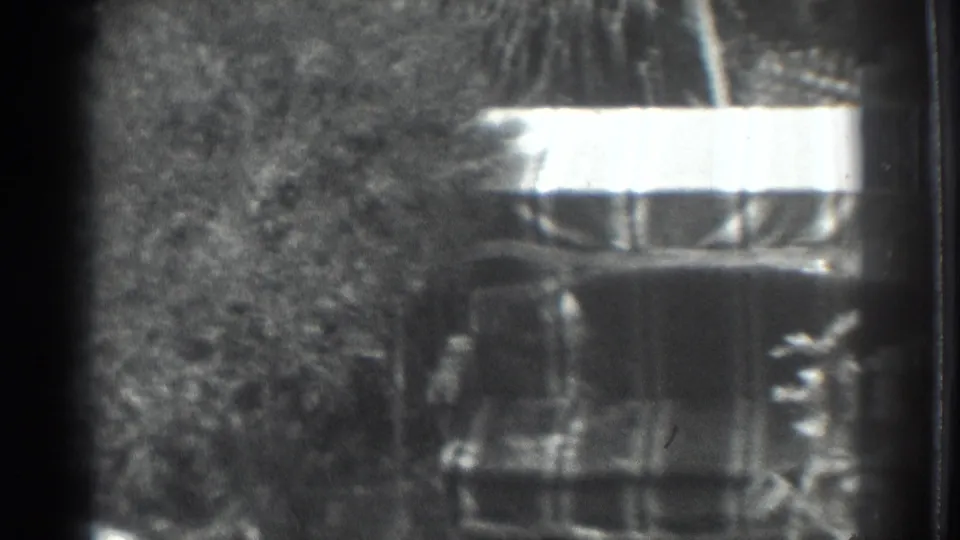 1937 Vacaville 8mm frame with trees, brush, and a bright-topped shaded structure or object in a rural outdoor setting.
