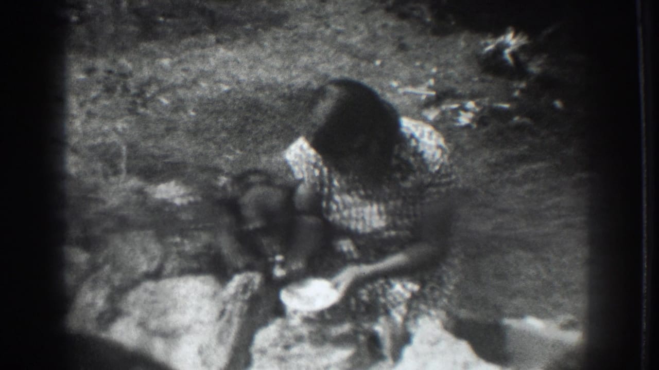 1937 Vacaville home-movie frame of a woman crouching in a rural yard while offering food from a bowl to a dark-furred dog.