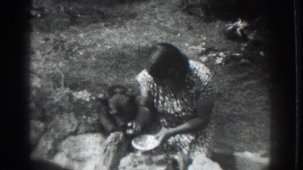 1937 Vacaville 8mm frame showing a woman in a patterned dress crouched beside a dark dog eating from a bowl outdoors.