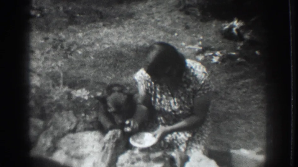 1937 Vacaville 8mm frame showing a woman in a patterned dress crouched beside a dark dog eating from a bowl outdoors.