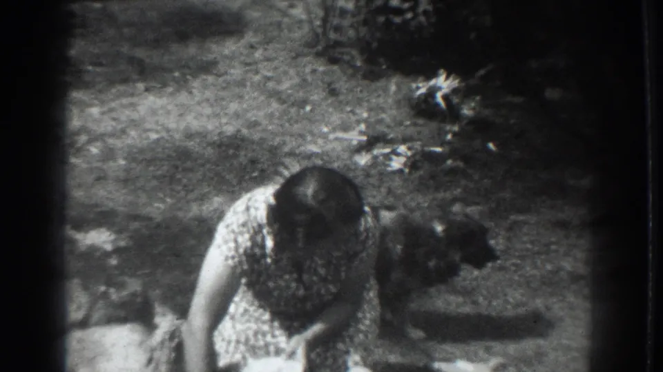 The woman remains bent forward in a Vacaville yard as the small dog stands close behind her in the grainy 8mm frame.