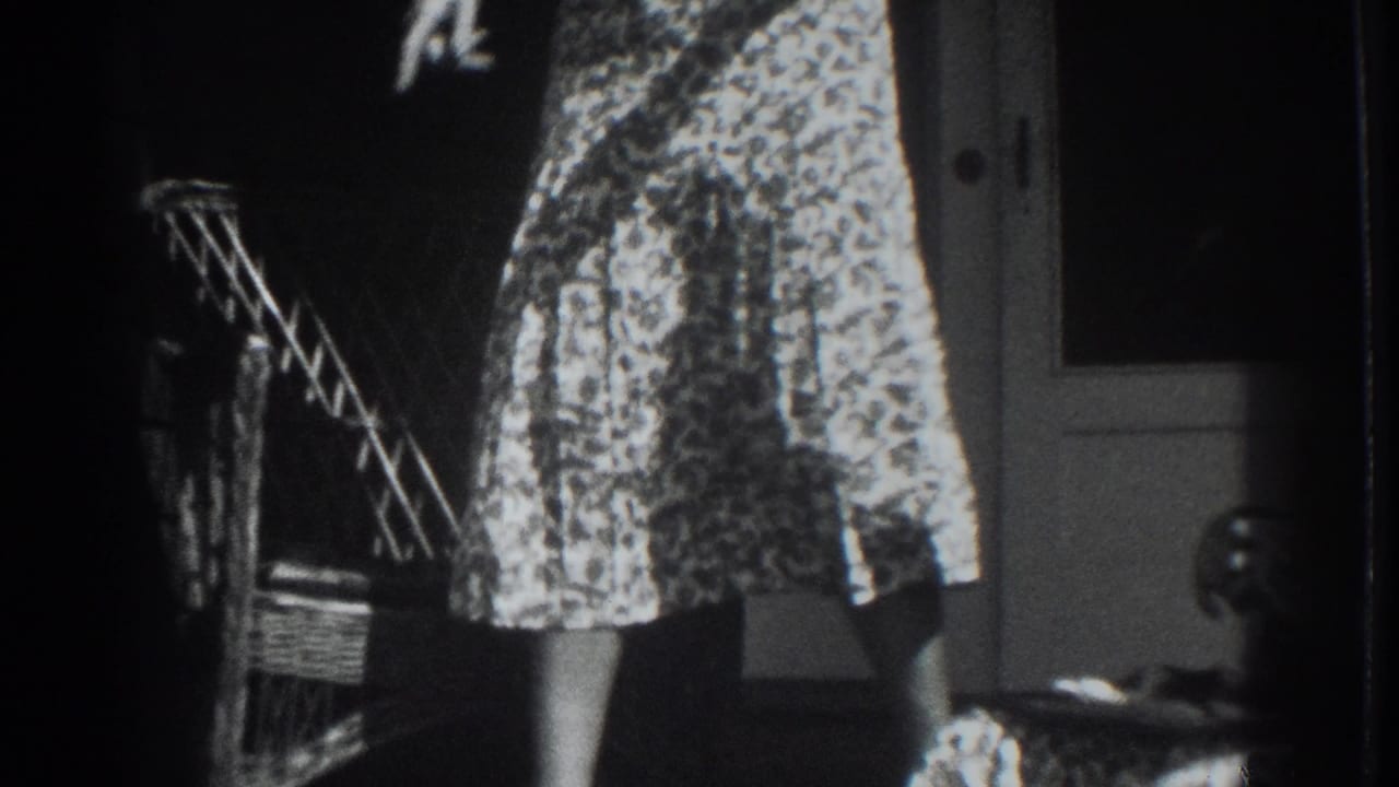 Woman in a patterned dress stands near a wicker chair and doorway.
