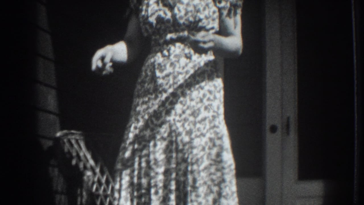 1937 Vacaville frame with a woman in a patterned dress holding a small possible animal or object near a porch doorway.