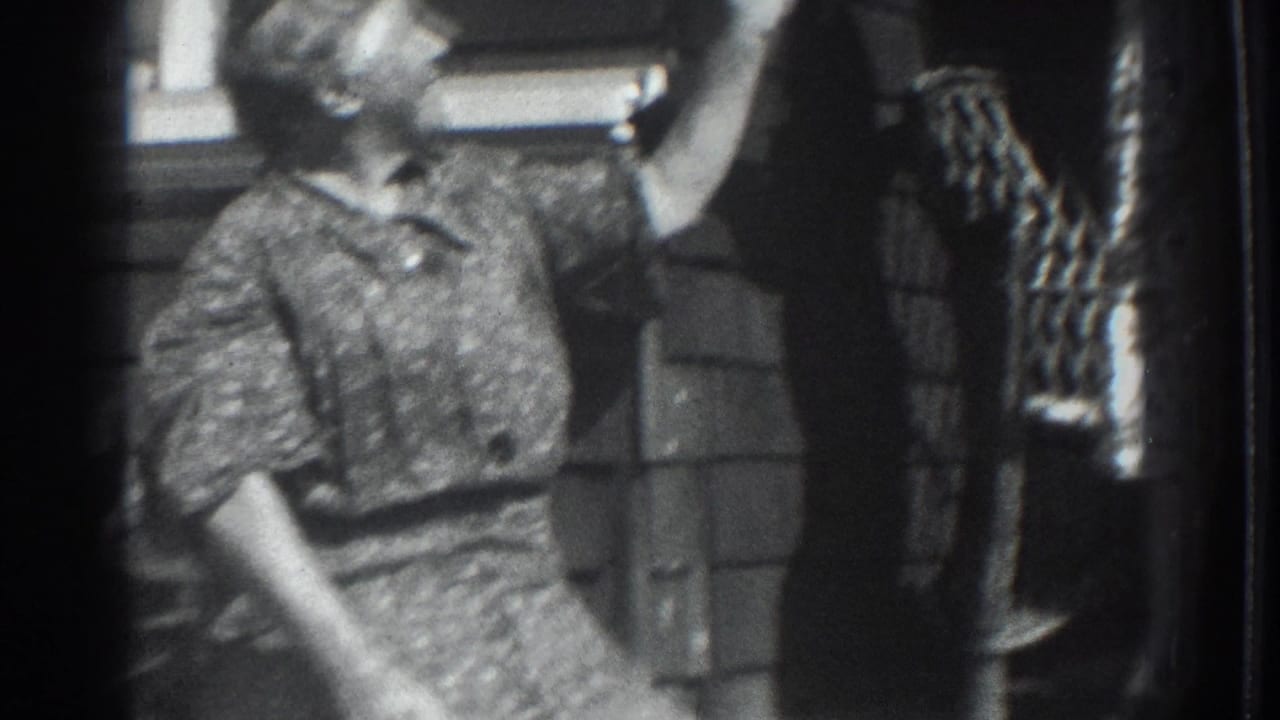 1937 Vacaville frame showing a young figure reaching up near a woman in a patterned dress at a home exterior.