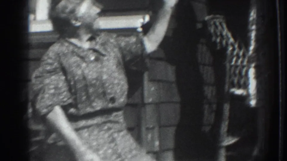 1937 Vacaville frame showing a young figure reaching up near a woman in a patterned dress at a home exterior.