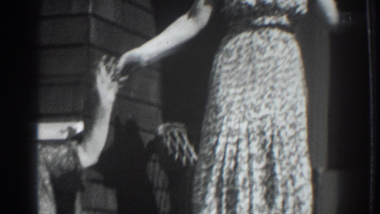 Vacaville, California home-movie frame from 1937 showing a woman in a patterned dress on a porch with another person waving at the edge.