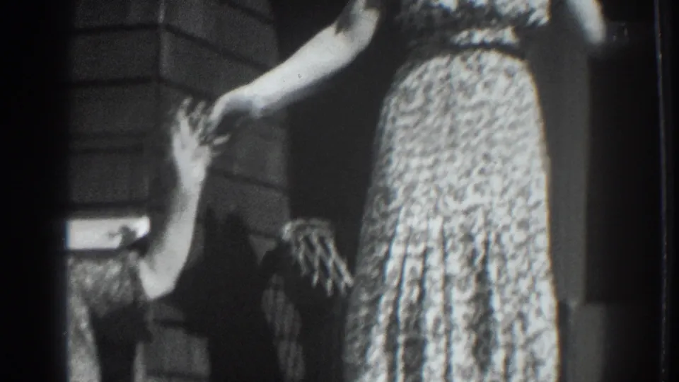Vacaville, California home-movie frame from 1937 showing a woman in a patterned dress on a porch with another person waving at the edge.
