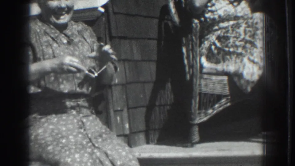 1937 Vacaville home-movie frame showing a seated woman on a porch with wicker furniture and another woman partly visible nearby.