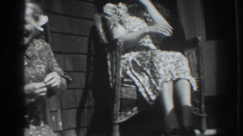 Vacaville 1937 frame showing adult women seated on a porch, including one in a light patterned dress beside shingled siding.