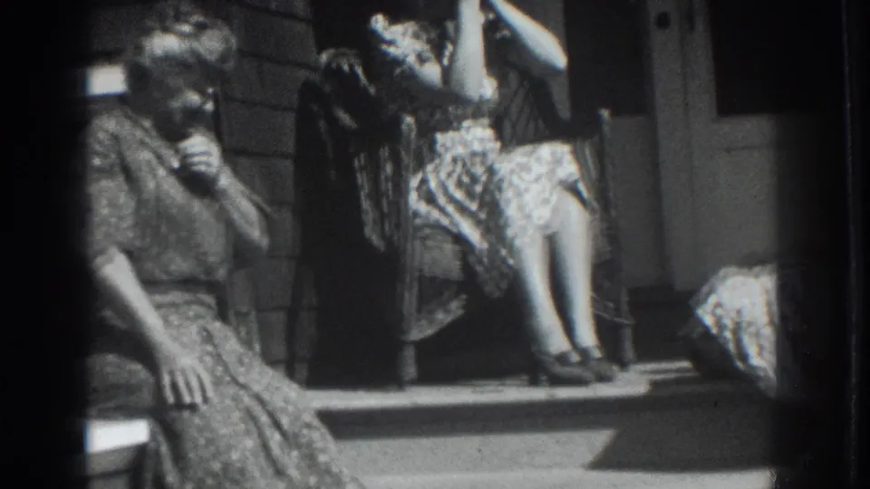 Two women in patterned dresses sit on a Vacaville porch in 1937, with one on the steps and another seated in a wicker chair near the doorway.