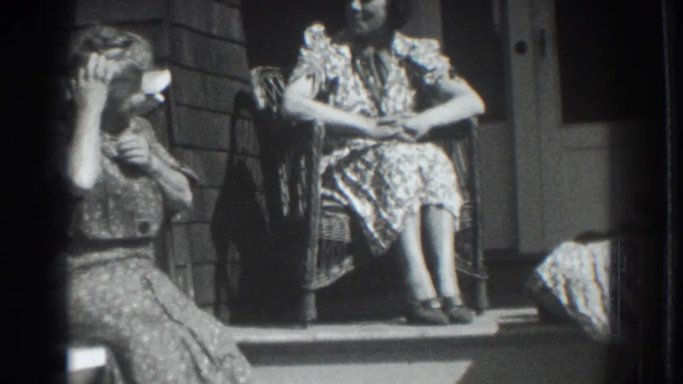 Near the end of the clip, two women sit on a sunlit Vacaville porch beside a doorway, with visible 8mm frame edges and soft grain.
