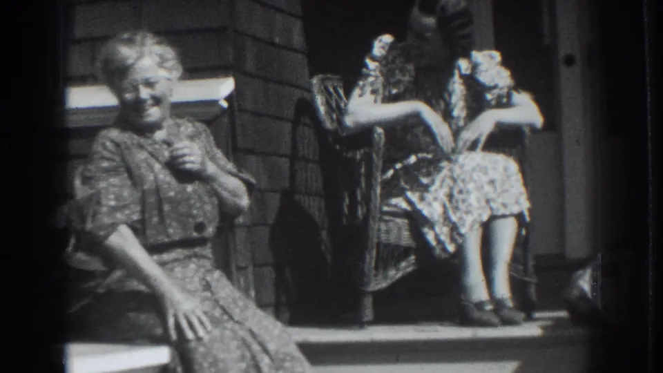 In 1937 Vacaville, a smiling woman sits in the foreground on porch steps while another woman sits higher beside a wicker chair.