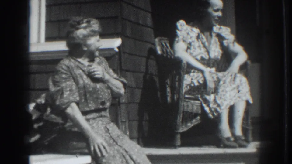 One woman gestures from the porch step while another sits in a wicker chair in Vacaville, California, 1937.