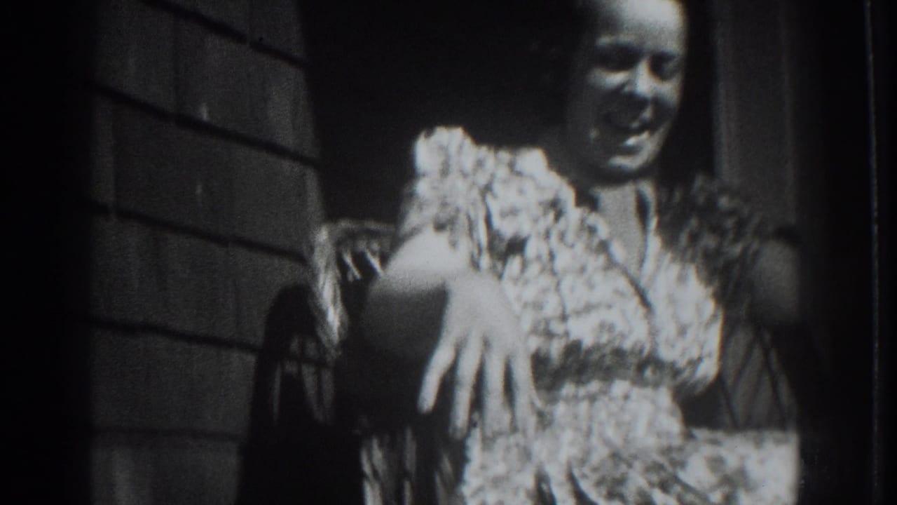 Adult woman in a patterned dress smiling from a wicker chair on a porch.