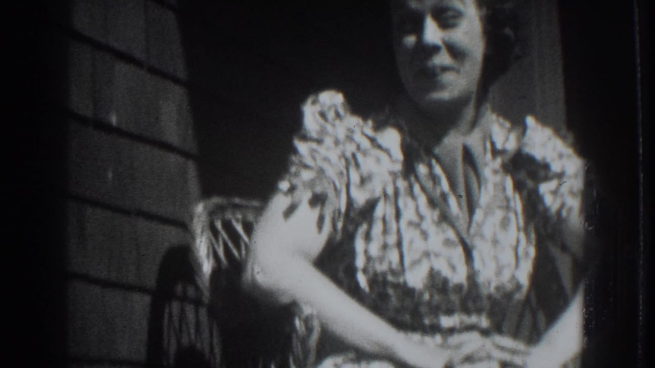 Woman in a patterned dress seated on a porch chair with hands clasped.