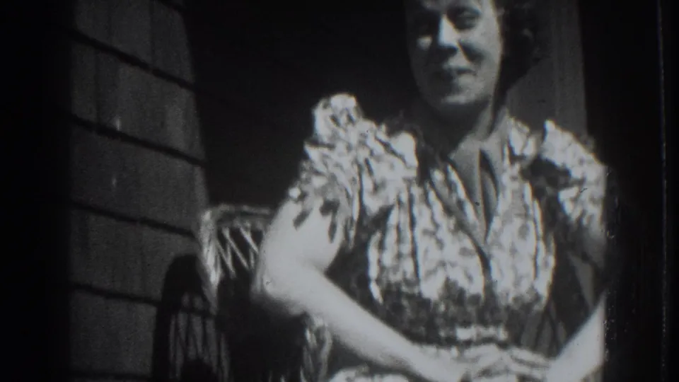 In 1937 Vacaville home-movie footage, a woman in a patterned dress sits on a porch chair against a shingled wall.