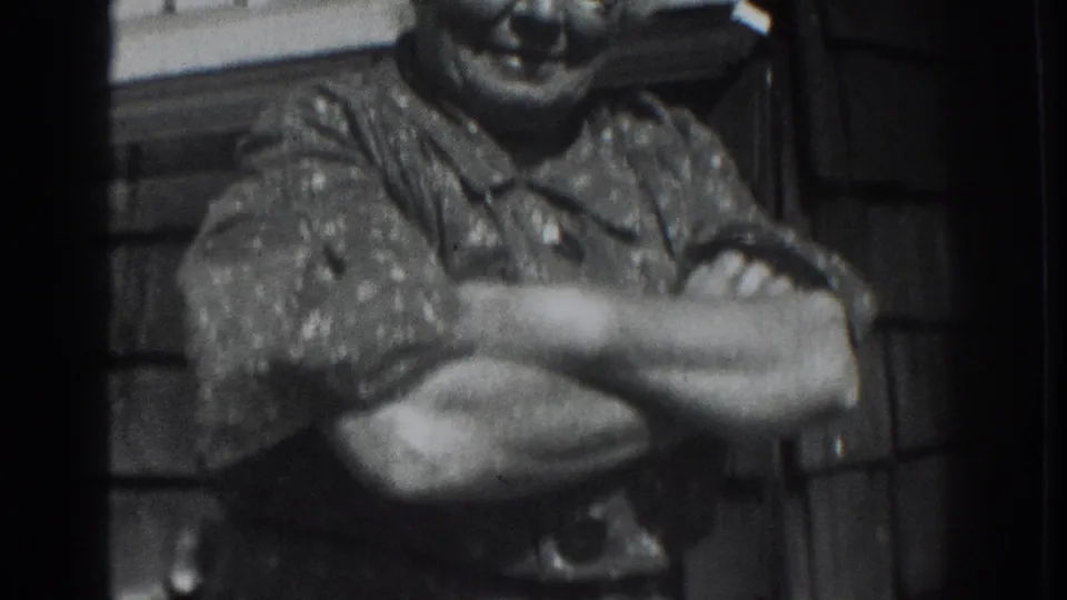 A smiling older woman in a patterned shirt stands with arms crossed outside a shingled house in Vacaville, California.